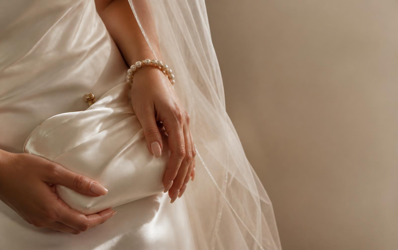 Bride holding an ivory satin clutch with a pearl bracelet